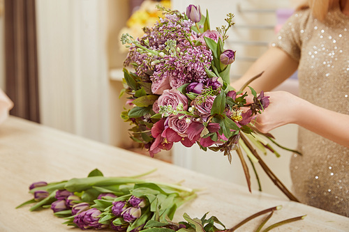 cropped view of florist making bouquet of tulips, peonies and lilac at workspace