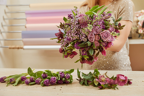 cropped view of florist making bouquet of purple tulips, peonies and lilac at flower shop