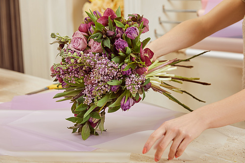 cropped view of florist wrapping  bouquet of tulips, peonies and lilac