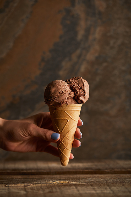 cropped view of woman holding chocolate ice cream cone over wooden table