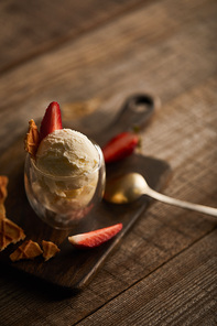 selective focus of delicious ice cream with strawberries in glass and spoon on wooden table