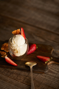 ice cream with strawberries and waffle pieces in glass and spoon on wooden table with copy space