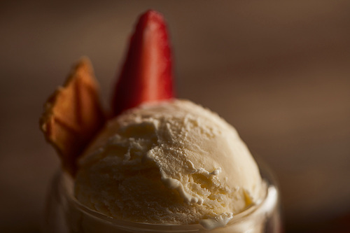 close up view of delicious ice cream scoop with piece of waffle and strawberry in glass