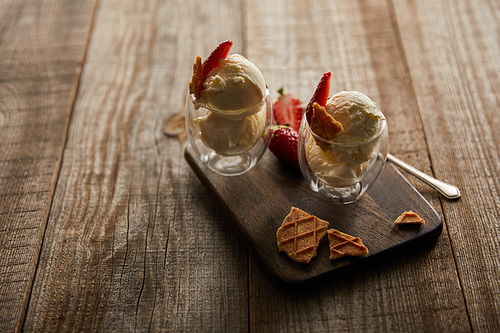 delicious ice cream in glasses with strawberries and pieces of waffle on cutting board on wooden table