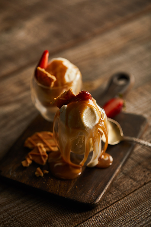 delicious ice cream with strawberries and caramel in glasses on chopping board