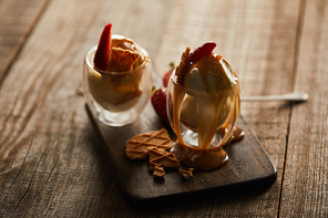 delicious ice cream in glasses with strawberries and caramel on wooden cutting board