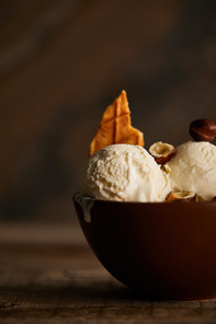 selective focus of delicious ice cream scoops with piece of waffle and hazelnuts in bowl on table