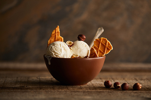 tasty ice cream scoops with pieces of waffle and hazelnuts in bowl on wooden table