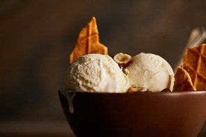 selective focus of delicious ice cream scoops with pieces of waffle and hazelnuts in bowl on table