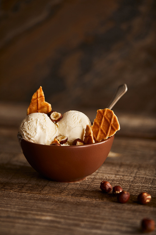 delicious ice cream scoops with pieces of waffle and hazelnuts in bowl on wooden table