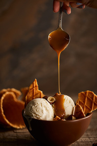 Cropped view of woman pouring caramel on ice cream with pieces of waffle and hazelnuts