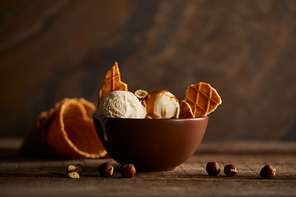 delicious ice cream with pieces of waffle and hazelnuts in bowl on wooden surface