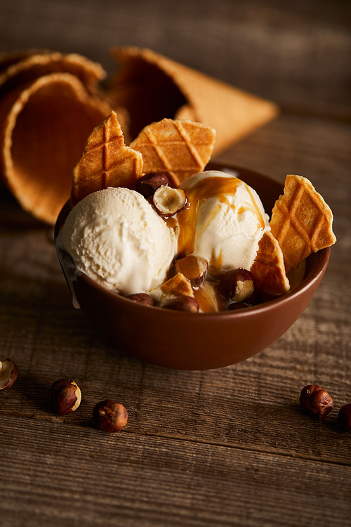 delicious ice cream with pieces of waffle and hazelnuts in bowl on wooden table