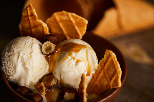 close up of delicious ice cream with pieces of waffle, caramel and hazelnuts in bowl