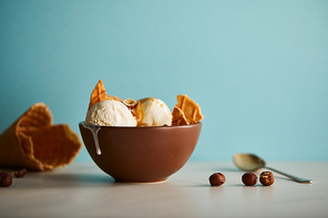 bowl of delicious ice cream with pieces of waffle and hazelnuts on blue
