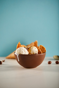 bowl of delicious ice cream with pieces of waffle and carmel on blue with copy space