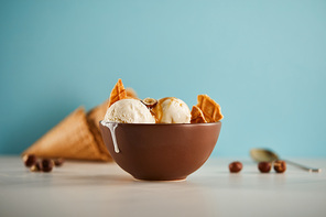 selective focus of bowl with delicious ice cream scoops with pieces of waffle on blue
