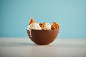 selective focus of bowl with delicious melting ice cream scoops and pieces of waffle on blue