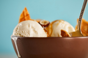 close up view of bowl with delicious ice cream with pieces of waffle and spoon on blue