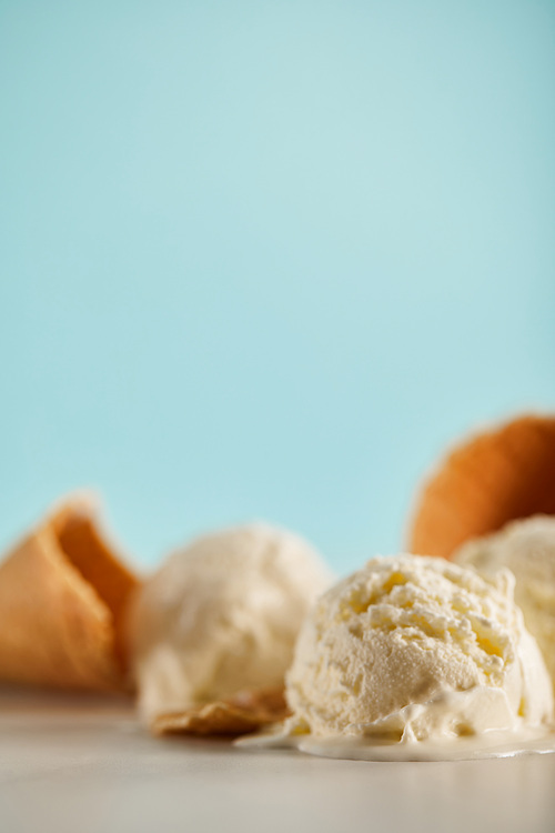selective focus of ice cream scoops and waffle cones on blue with copy space