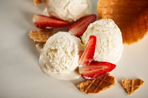 close up view of waffle pieces and delicious melting ice cream with strawberries on grey
