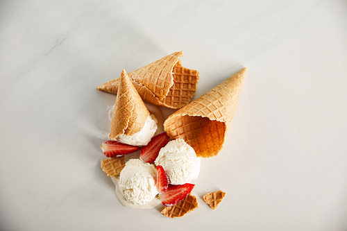 top view of cones and delicious melting ice cream with strawberries on grey surface