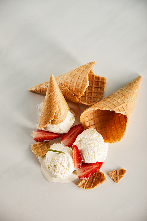 top view of waffle cones and delicious melting ice cream with strawberries on grey