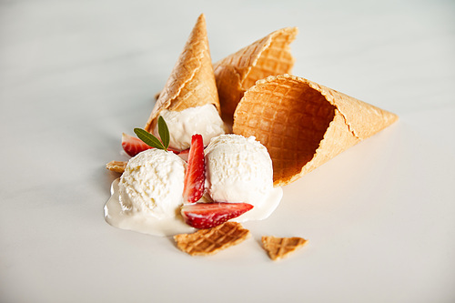 waffle cones and delicious melting ice cream with strawberries on grey table