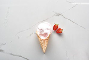top view of tasty ice cream in waffle cone near strawberries on marble grey background