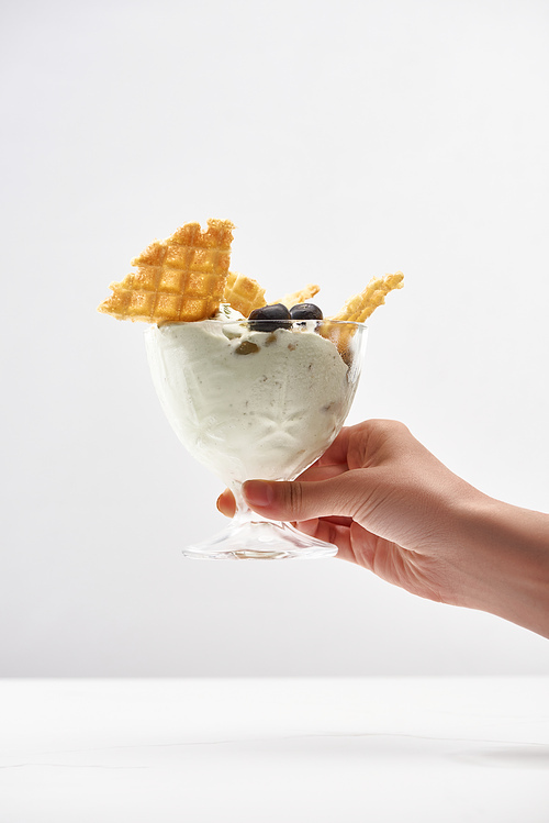 cropped view of woman holding delicious pistachio ice cream with waffles and blueberries isolated on grey