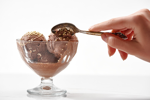 cropped view of woman holding spoon near delicious chocolate ice cream in glass bowl isolated on white