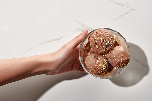 partial view of woman holding delicious chocolate ice cream in bowl on marble grey background