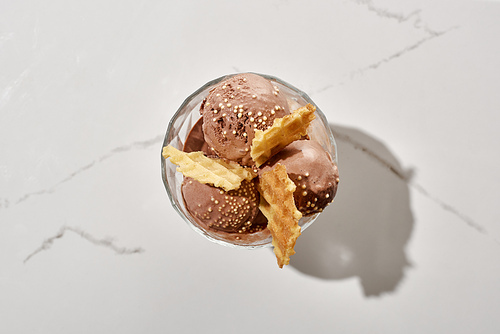 top view of delicious chocolate ice cream in bowl with waffles on marble grey background