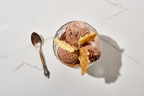 top view of spoon and delicious chocolate ice cream in bowl with waffles on marble grey background