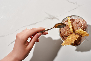 cropped view of woman holding soon near delicious chocolate ice cream in bowl with waffles on marble background