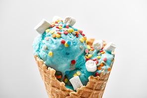 close up view of delicious sweet blue ice cream with marshmallows and_sprinkles in crispy waffle cone isolated on grey