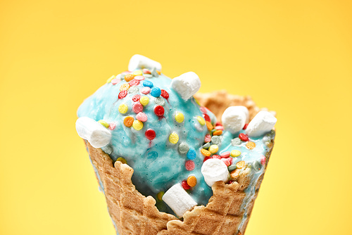 close up view of delicious sweet blue ice cream with marshmallows and_sprinkles in crispy waffle cone isolated on yellow