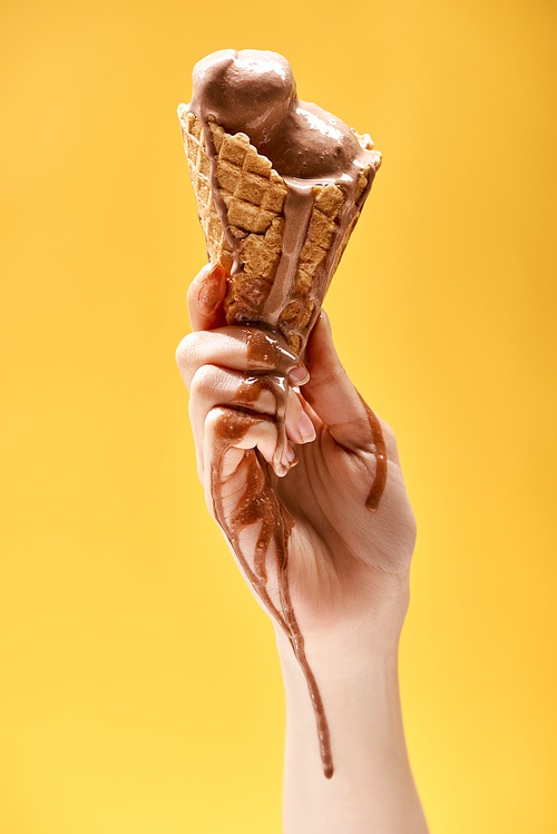 partial view of woman holding delicious melted chocolate ice cream in crispy waffle cone isolated on yellow