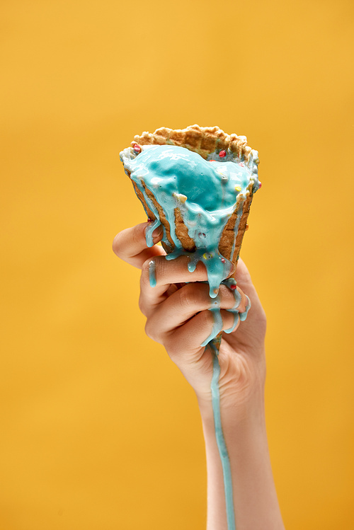 cropped view of woman holding melted blue ice cream in crispy waffle cone isolated on yellow