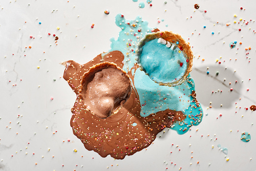 top view of delicious melted chocolate and blue ice cream in waffle cones on marble grey background with sprinkles