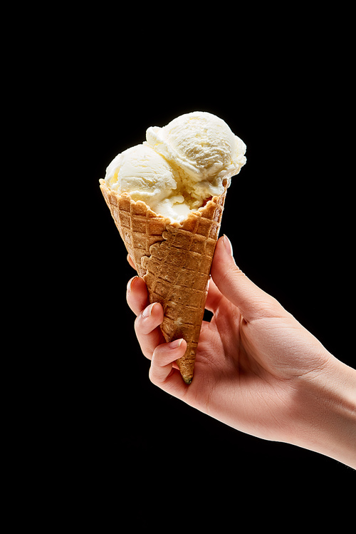 cropped view of woman holding delicious vanilla ice cream in crispy waffle cone isolated on black