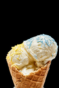 close up view of delicious vanilla ice cream with sprinkles in crispy waffle cone isolated on black