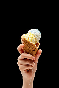 cropped view of woman holding delicious vanilla ice cream with sprinkles in crispy waffle cone isolated on black