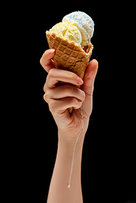 cropped view of woman holding melting delicious vanilla ice cream with sprinkles in crispy waffle cone isolated on black