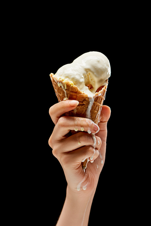 cropped view of woman holding melting delicious vanilla ice cream in crispy waffle cone isolated on black