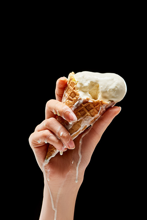 partial view of woman holding melting delicious vanilla ice cream in crispy waffle cone isolated on black