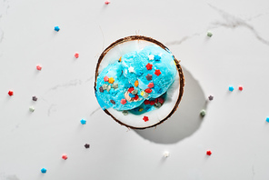 top view of delicious blue ice cream with sprinkles on coconut half on marble grey background