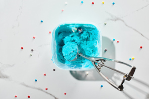 top view of delicious blue ice cream with sprinkles in box with ice cream spoon on marble grey background