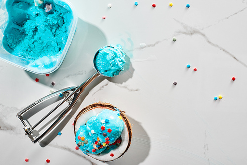 top view of delicious blue ice cream with sprinkles on coconut half and in ice cream spoon on marble grey background