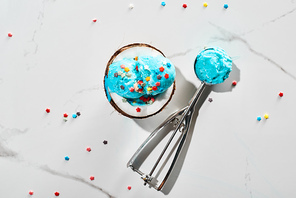 top view of fresh blue ice cream with sprinkles on coconut half and in ice cream spoon on marble grey background